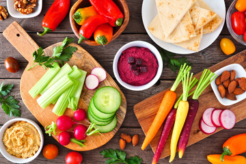 Table scene with a variety of fresh vegetables and hummus dips. Overhead view on a rustic wood...