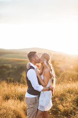 Handsome man and pretty woman in stylish boho rustic clothes, kissing. Lovely couple in eco boho rustic style, standing in summer field. Kissing sensual moment