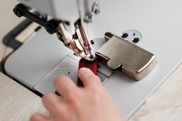 The hands of a master and the needle of a leather product sewing on a sewing machine. Manual work, business.