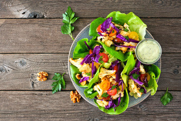 Healthy lettuce wraps with grilled cauliflower, cabbage and tomatoes. Above view over a rustic wood background. Plant-based diet concept. - obrazy, fototapety, plakaty