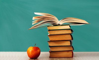 Back to school, pile of books and red apple with empty school board background, education concept.