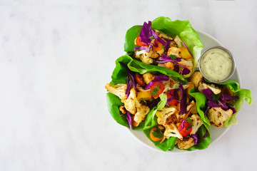 Healthy lettuce wraps with grilled cauliflower, cabbage and tomatoes. Top view over a white marble...