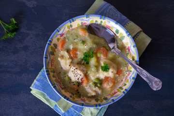 Bowl of chicken stew with vegetables on dark gray background. Overhead horizontal image