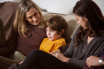 Obraz premium Boy sitting with smiling mother and grandmother on sofa at home