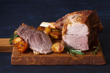 Roast leg of lamb with potatoes and rosemary on serving wooden board