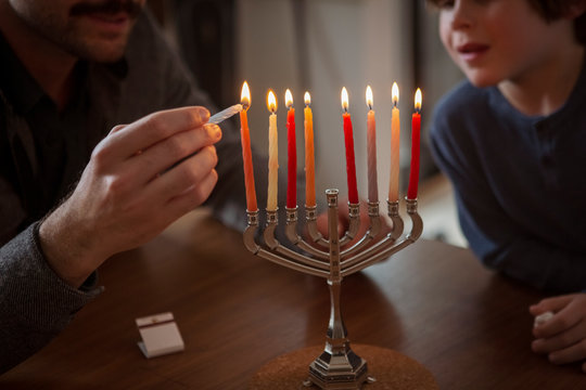 Midsection of boy looking at father burning candles on menorah at home during Hanukkah festival