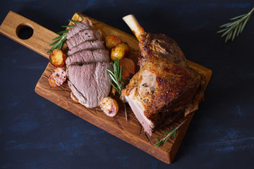 Roast leg of lamb with potatoes and rosemary on serving wooden board. View from above, top view