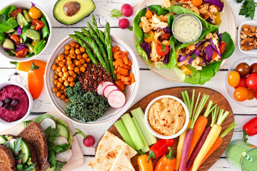 Healthy lunch table scene with nutritious Buddha bowl, lettuce wraps, vegetables, sandwiches and salad. Top view over a white wood background.