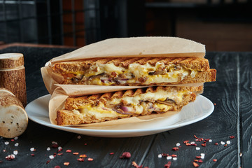 Appetizing veggie club-sandwich in toast bread with melted cheese, red onion, mushrooms in craft paper on a black wooden background