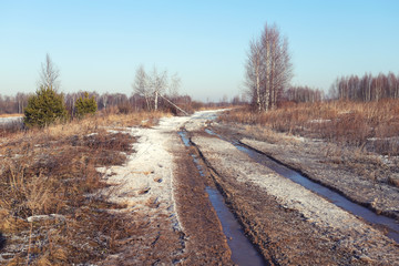 Fototapeta premium Landscape in early spring in the field. Dirty road with melting snow on a sunny day.