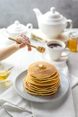 A stack of pancakes with honey in a light key