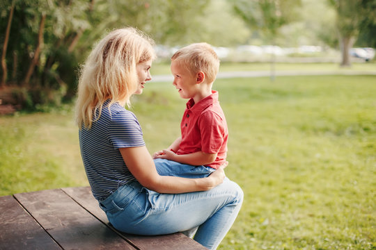 Young Caucasian Mother And Boy Toddler Son Sitting Together Face To Face. Family Mom And Child Talking Communicating Outdoor On A Summer Day. Happy Authentic Family Childhood Lifestyle.