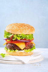 Close-up of a tasty hamburger sandwich containing: cooked patties of ground meat, onion, tomatoes, cheese, fresh green salad, sauce on a light background, space for text. Fast food concept, burger.
