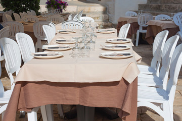 Empty restaurant  in the summer time in Italy. Holidays in Europe. Table with plates and glasses for wine and water, serving napkins, chairs near the table