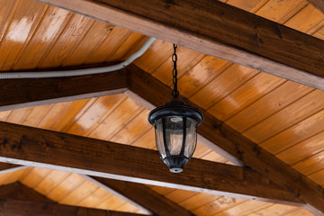 A lantern with iron fixtures to the wall and a glass canopy mounted on a wooden log house.