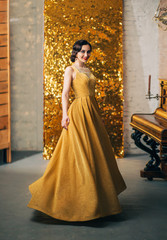Beautiful young woman finger wave hairstyle in long luxurious elegant gold dress smiles bright...