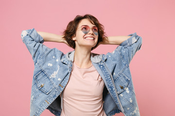 Smiling young brunette woman girl in casual denim jacket eyeglasses posing isolated on pastel pink wall background. People lifestyle concept. Mock up copy space. Looking up with hands behind head.