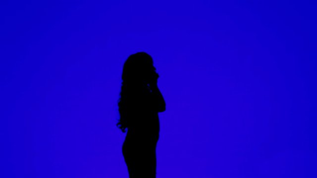 Silhouette of a young woman with curly hair talking on a cell phone on a blue background