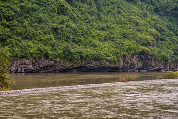 Guilin, China - May 10, 2010: Along Li River. Forested green karst mountain slope recede at bottom on greenish water level. 