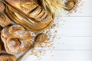 Traditional wheat bread, rolls and ears of cereals on a white wooden background