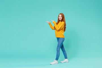 Pretty young redhead woman girl in yellow sweater posing isolated on blue turquoise background studio portrait. People emotions lifestyle concept. Mock up copy space. Pointing index fingers aside.