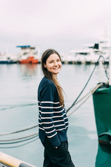 Beautiful happy cheerful laughing young woman in casual clothes. One person in the landscape of the seaport.