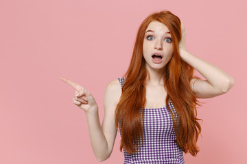 Shocked young redhead woman girl in plaid dress posing isolated on pastel pink background studio portrait. People lifestyle concept. Mock up copy space. Pointing index finger aside, put hand on head.