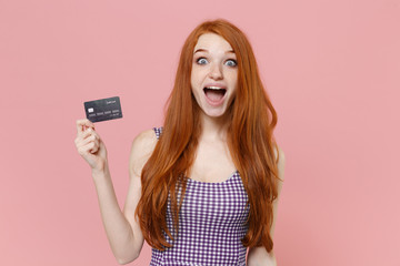 Surprised young redhead woman girl in plaid dress posing isolated on pastel pink wall background studio portrait. People sincere emotions lifestyle concept. Mock up copy space. Hold credit bank card.