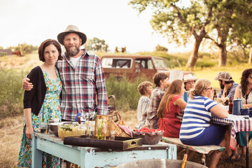 Couple stand in front of picnic table set with loads of great food in the outdoors. Bridger, Montana, USA