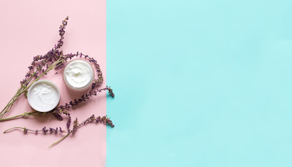 Fototapeta premium Concept of natural beauty products. With white cream and lavender flower for skin care on a pastel blue background with green leaves. Top view and copy space Flat lay.