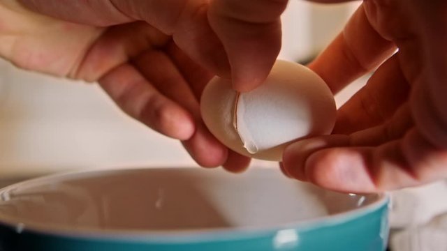 eggs cracking in bowl slow motion - male hands crack egg and pour into teal bowl in kitchen with shallow depth of field