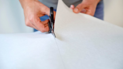 closeup male hands preparing new bended wallpaper roll with scissors on table indoor