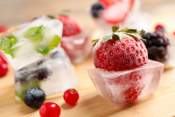 Ice cubes with different berries and mint on wooden board, closeup