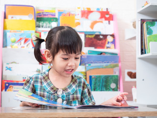 Fototapeta premium Asian little cute girl sitting and reading the tale book on table. Preschool lovely kid reading the book. Learning and education of kid.