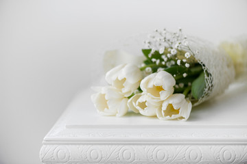 Fototapeta na wymiar bouquet of white tulips on an antique white furniture - white background, selective focus
