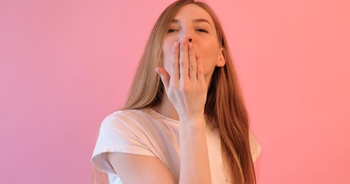 beautiful girl in a white t-shirt sends a kiss, on a pink background