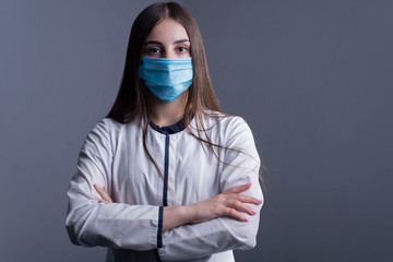 Closeup portrait of a young girl. doctor in a white coat, and a medical mask. looking at the camera. Studio photo on a gray background.