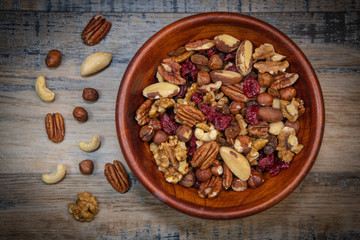 Mixed nuts and dried fruits in wooden bowl on wood background, copy space