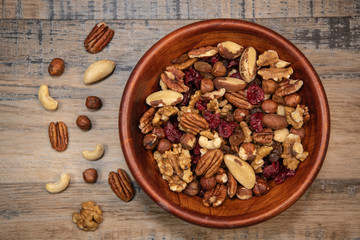 Mixed nuts and dried fruits in wooden bowl on wood background, copy space