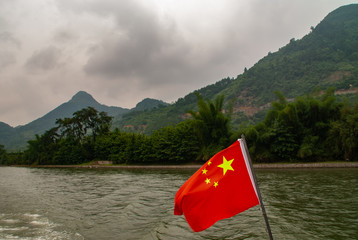 Guilin, China - May 10, 2010: Along Li River. Closeup of Blood red Chinese flag and the green...
