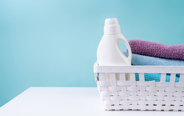 Laundry basket with a detergent bottle and a pile of clean towels on white table isolated on blue...