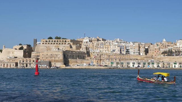 City skyline of Valletta in Malta, sea view with traditional Luzzu boat and group of unidentified tourists on sightseeing tour in the Grand Harbour