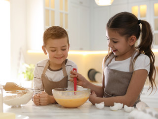 Cute little children cooking dough together in kitchen