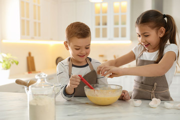 Cute little children cooking dough together in kitchen