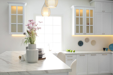 Fototapeta na wymiar Beautiful flowers and dishware on white marble table in modern kitchen