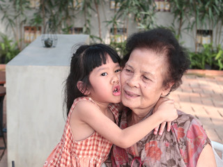A little girl has her warm grandmother in  arms and they touch together with love.
