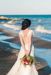 Brunette bride in light chiffon wedding dress embroidered with beads posing near the sea. Romantic...