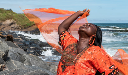 African woman with orange dress on the cliffs by the sea in Sekondi-Takoradi Ghana West Africa
