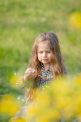 Cute little blonde girl blowing soap bubbles having fun in the spring park.