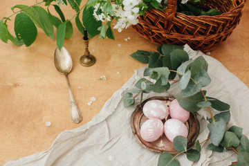 Modern Easter eggs with eucalyptus branch on rustic wooden table with basket and candle. Stylish pastel pink Easter eggs painted in natural dye from beets. Happy Easter